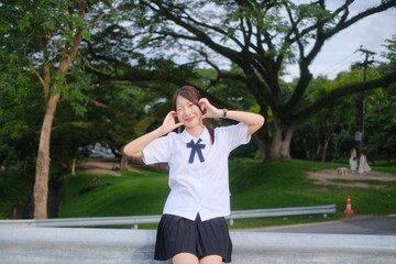 A girl in a school uniform is sitting on a bench in a park. A Student girl concept