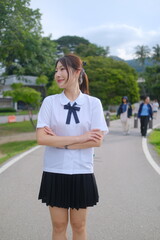 A woman in a school uniform stands on a sidewalk with her arms crossed. A Student girl concept