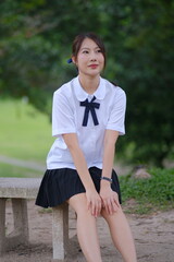 A young woman wearing a white shirt and black skirt sits on a bench. A Student girl concept