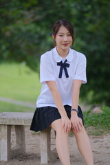 A young woman is sitting on a bench wearing a school uniform. A Student girl concept