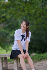 A young woman wearing a school uniform and a bow tie sits on a bench in a park. A Student girl...