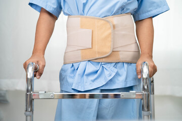 Asian senior pain back wearing elastic support belt with walker.