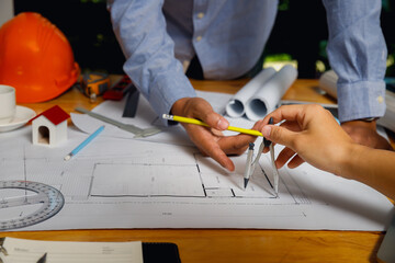 Close-up of engineers collaborating on architectural blueprint with pencil and compass, focusing on...