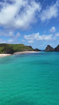 Morro Dois Irm&atilde;os em Fernando de Noronha: duas eleva&ccedil;&otilde;es rochosas erguidas no mar turquesa, com recifes vis&iacute;veis e ondas quebrando nas bases