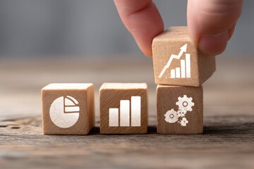 Wooden blocks with business icons, hand placing a block with an upward trend graph
