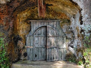 Fototapeta premium Old wooden door embedded in rocky cave wall, creating a mysterious entrance. Worn texture and natural surroundings evoke a sense of hidden history and adventure.