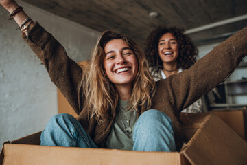 Two cheerful women sharing laughter while sitting inside a cardboard box during moving day