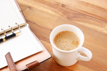 Opened schedule planner, diary, notebook with cup of Coffee on table
