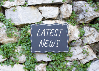 Latest News symbol. Stone wall with words Latest News. Beautiful stone background with plants....