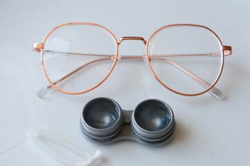 eyeglasses with gold frame, contact lens case and tweezers on white surface, vision correction, eye...