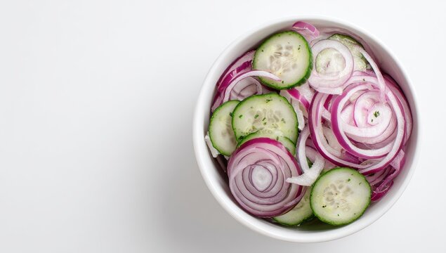 A white bowl filled with thinly sliced red onions and cucumbers, arranged artfully, sits on a white background