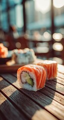 Two salmon avocado sushi rolls sit on a rustic wooden table outdoors in warm sunlight; blurred background shows more sushi and an out-of-focus cityscape