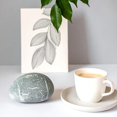 Smooth grey stone beside a cup of coffee and a grayscale leaf print
