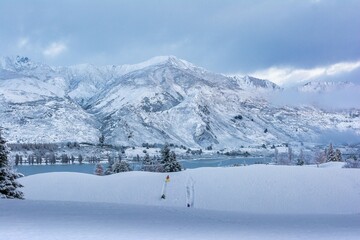 Winter landscape of snow-covered mountains and trees reflected in a tranquil lake in Wanaka, NZ