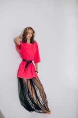 The model is a young beautiful girl in a pink dress with a transparent skirt in a studio on a white...