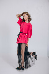 The model is a young beautiful girl in a pink dress with a transparent skirt in a studio on a white...
