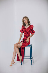 The model is a young beautiful girl in a red long dress in a studio on a white background