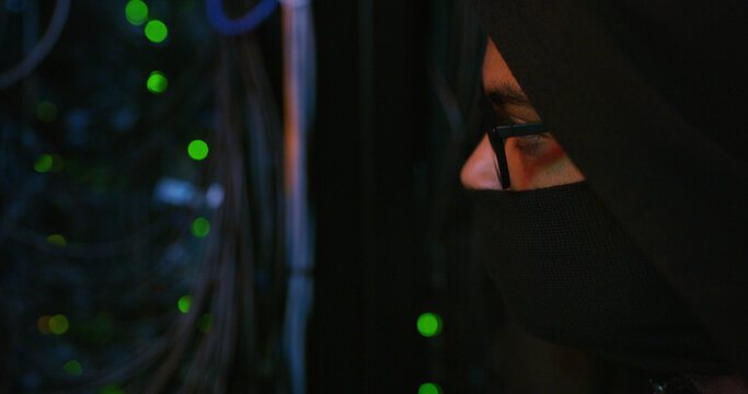 Night, hacker and person with mask by cables for scam, phishing or cybercrime for online attack. Anonymous, privacy and programmer with security breach, server or database encryption in control room.