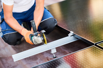 Worker installing or maintaining photovoltaic solar panel system on roof of house. Close up technician using grinder on metal part of the panel's mounting structure. Concept renewable energy.
