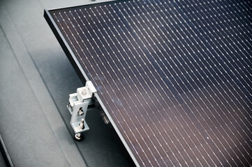 Close up of solar panel, securely fastened with robust mounting clamp to supporting structure on rooftop of house. Bolts and clamps provide stability and durability to solar installation.