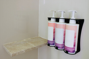 Dispenser with three bottles in a bathroom or shower setting.