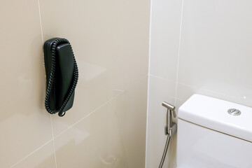 Wall-mounted telephone next to a modern toilet in a bathroom setting.