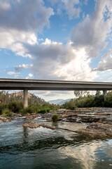 Scenic view of a river flowing under a bridge with a dramatic cloudy sky in a natural landscape