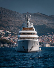 Large luxury yacht sailing on the blue sea with a coastal city and mountains in the background