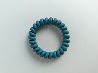Close-up of a teal coiled spiral hair tie on a white background, minimalist and isolated for product or accessory design concepts.