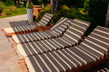 A row of empty sun loungers near a swimming pool, with fabric shade from a security fence at a...