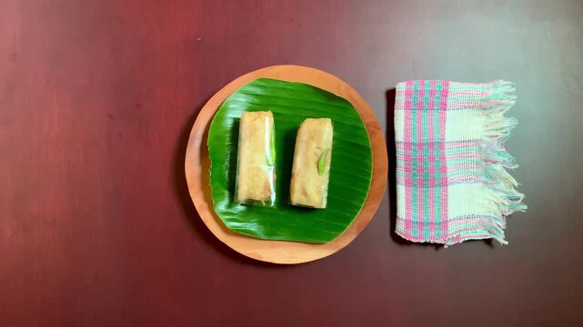4k close-up top angle of hand putting sosis solo on banana leaf wooden plate to the table, pink striped napkin beside. Bright natural light, ideal for food, culinary, and rustic lifestyle projects.