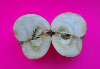 Two halves of a cut apple are placed side-by-side on a bright pink background, demonstrating...