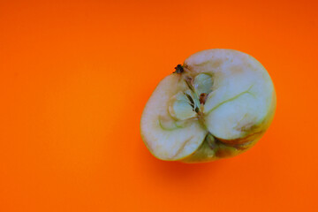 An apple, cut in half, lies on a bright orange background, showing its internal structure. The...