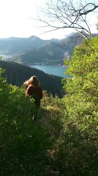 A female tourist descends the mountainside with a stunning view of the Bay of Kotor. Hiking trail on Mount Vrmac in Montenegro. Adventure, outdoor exploration, active lifestyle, nature travel concepts