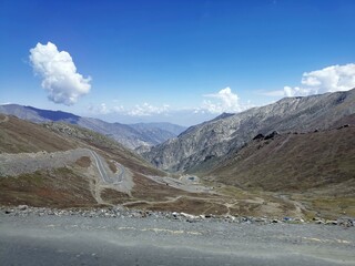 Spectacular mountain view featuring a curving road amid rugged terrain. The clear blue sky enhances...