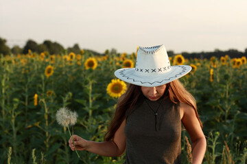 Young slim woman in jeans and hat in sunflower field