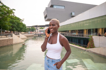 Young black woman talking on smartphone by the canal in urban setting