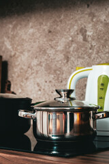 Steel pots on induction hob and kettle on cozy modern kitchen with cooking utensils, pots, cutting...