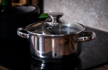 Steel pots on induction hob on cozy modern kitchen with cooking utensils, pots, cutting boards on...