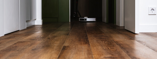 White robot vacuum cleaner mopping floors and vacuuming while cleaning in beautiful modern apartment