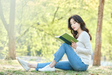 Obraz premium Young Asian female relaxing and reading a book outdoors in spring park