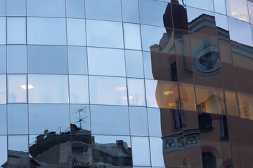 Old houses are reflected in the glass facade of the modern building