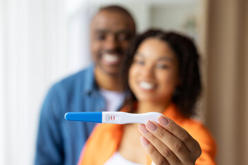 Closeup of positive pregnancy test held by smiling African American couple, showing happiness,...