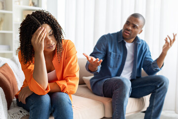 Frustrated African American couple arguing at home, woman feeling stressed, holding her head in...