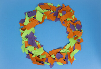 A close-up of torn orange, green and purple paper edges arranged diagonally, creating an abstract textured background.