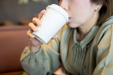 Close-up of a woman sipping coffee from a white paper cup.