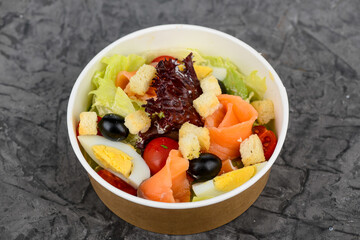 Fresh vegetable salad with salmon in a disposable dish on a gray background
