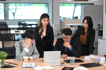 Overwhelmed coworkers analyzing data on a laptop with anxious expressions during a meeting