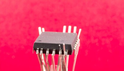 Close-up of a black square integrated circuit with numerous pins against a red backdrop