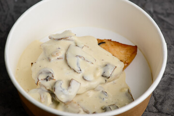 fried chicken fillet with creamy mushroom sauce in a disposable dish macro photo